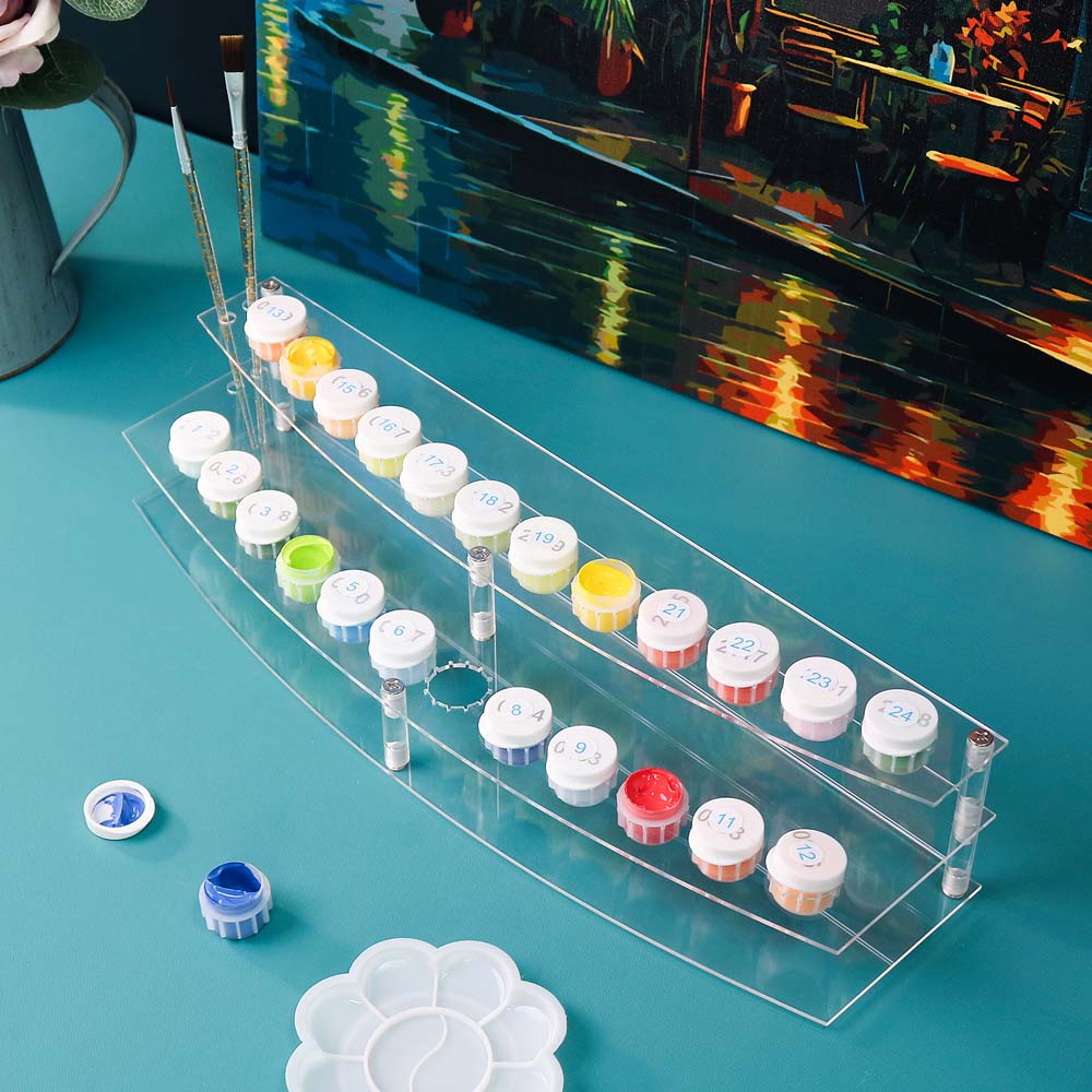 Clear acrylic paint organizer with various small containers on a blue surface.