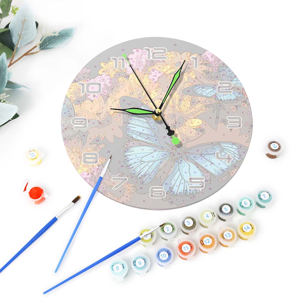 Decorative clock with butterfly design, surrounded by paint bottles and brushes on a white background