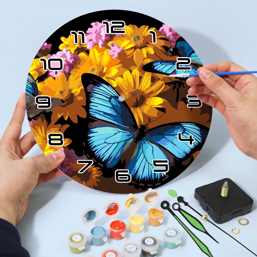 Decorative clock with butterfly and floral design, being painted by a person.