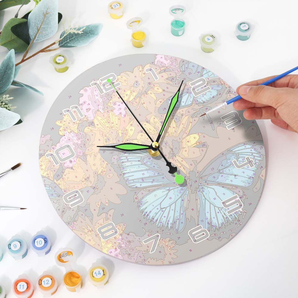 Person painting a butterfly design on a round clock with various paint containers and brushes around.