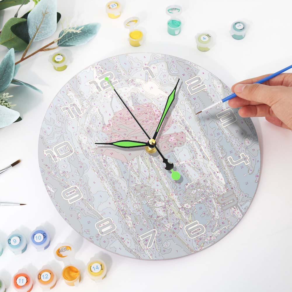 Person painting a round clock with various paint containers and brushes on a white surface.