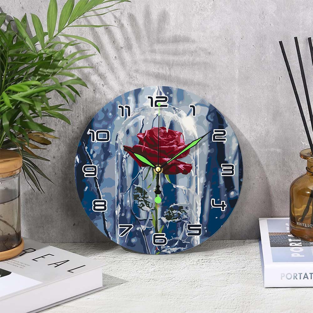 Decorative wall clock with a rose design on a gray surface with a plant and books.
