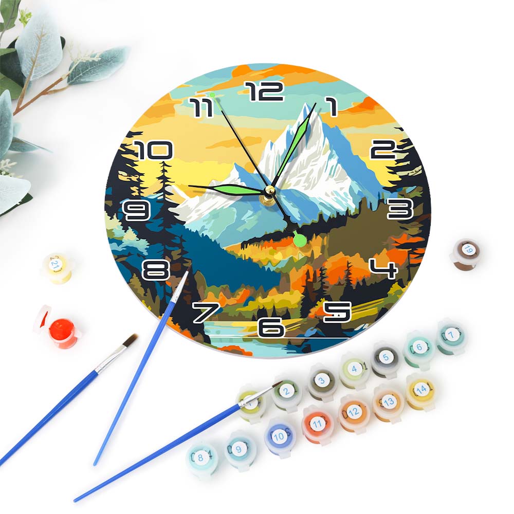Decorative clock with mountain design, surrounded by paint tubes and brushes on a white background