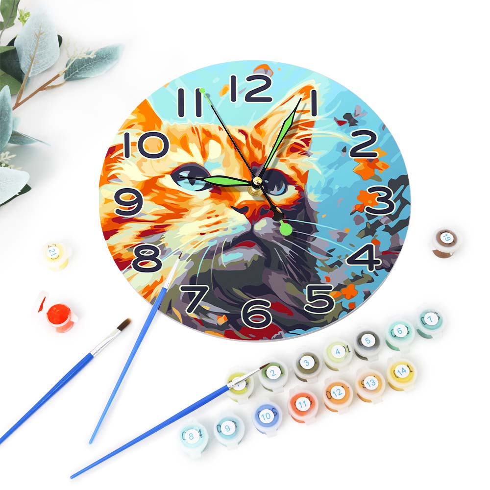 Clock with a cat design surrounded by art supplies on a white background