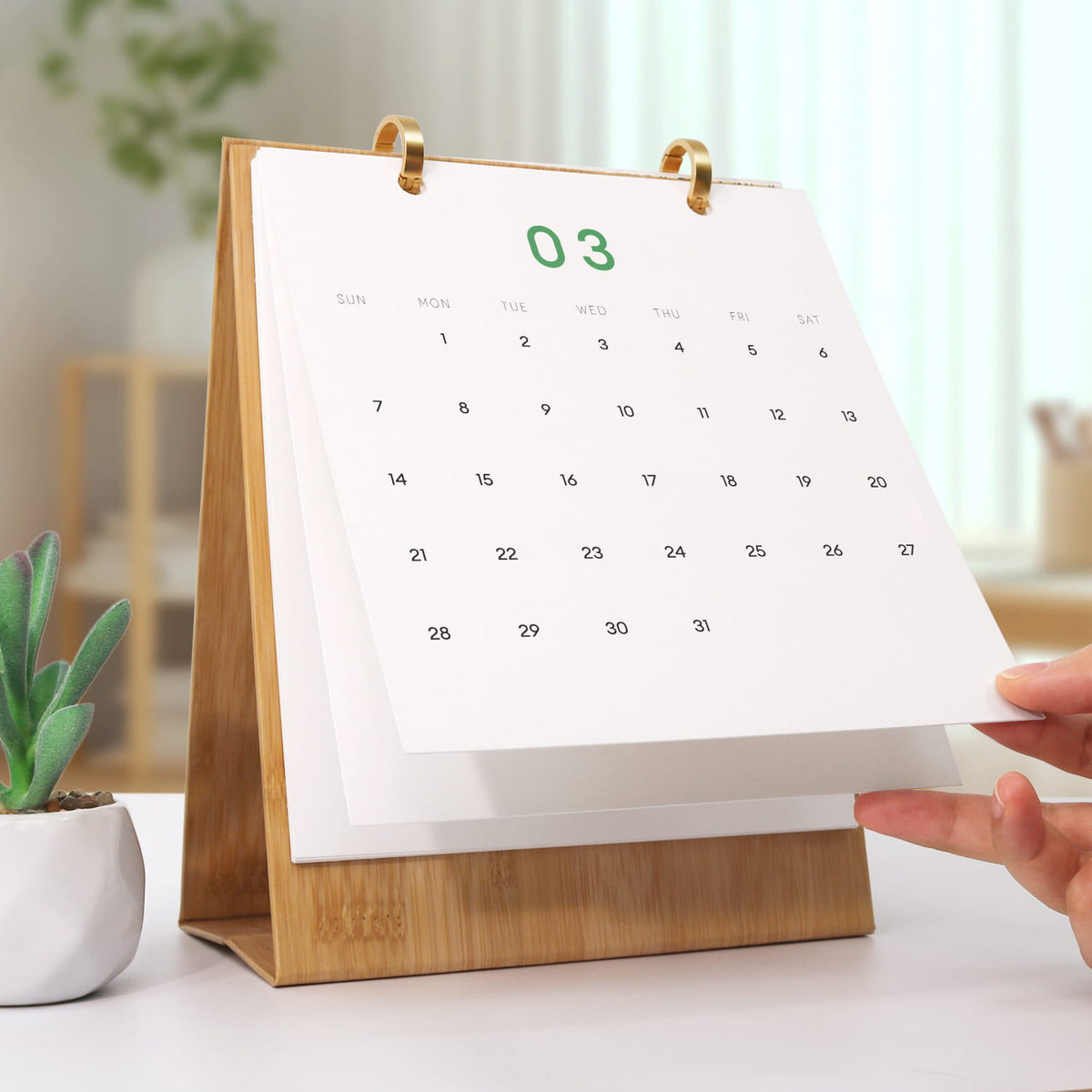 
Calendar with a wooden stand on a table, with a hand adjusting the page.