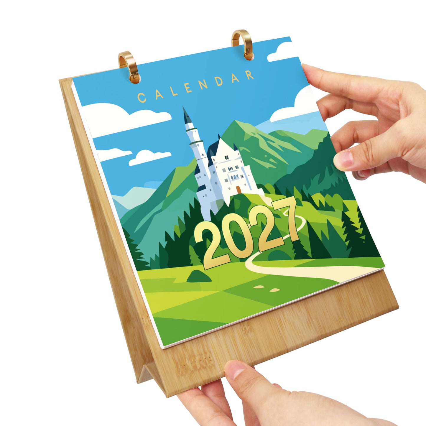 A bamboo desk calendar with a 2027 cover featuring a colorful illustration of Neuschwanstein Castle, held by two hands against a white background.