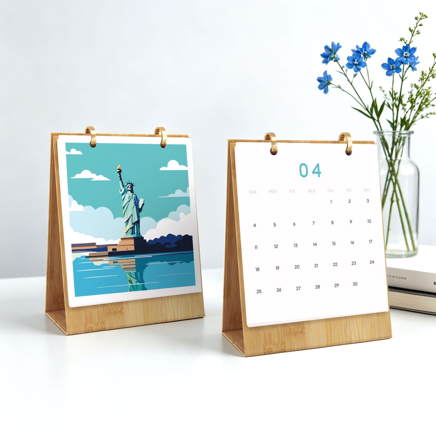 Two small wooden desktop calendar stands on a white surface. The left stand shows a stylized Statue of Liberty illustration with blue sky and water; the right stand shows a blank white page with the number 04 at the top.