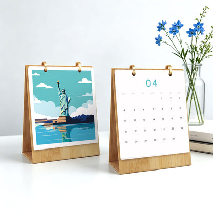 Two small wooden desktop calendar stands on a white surface. The left stand shows a stylized Statue of Liberty illustration with blue sky and water; the right stand shows a blank white page with the number 04 at the top.