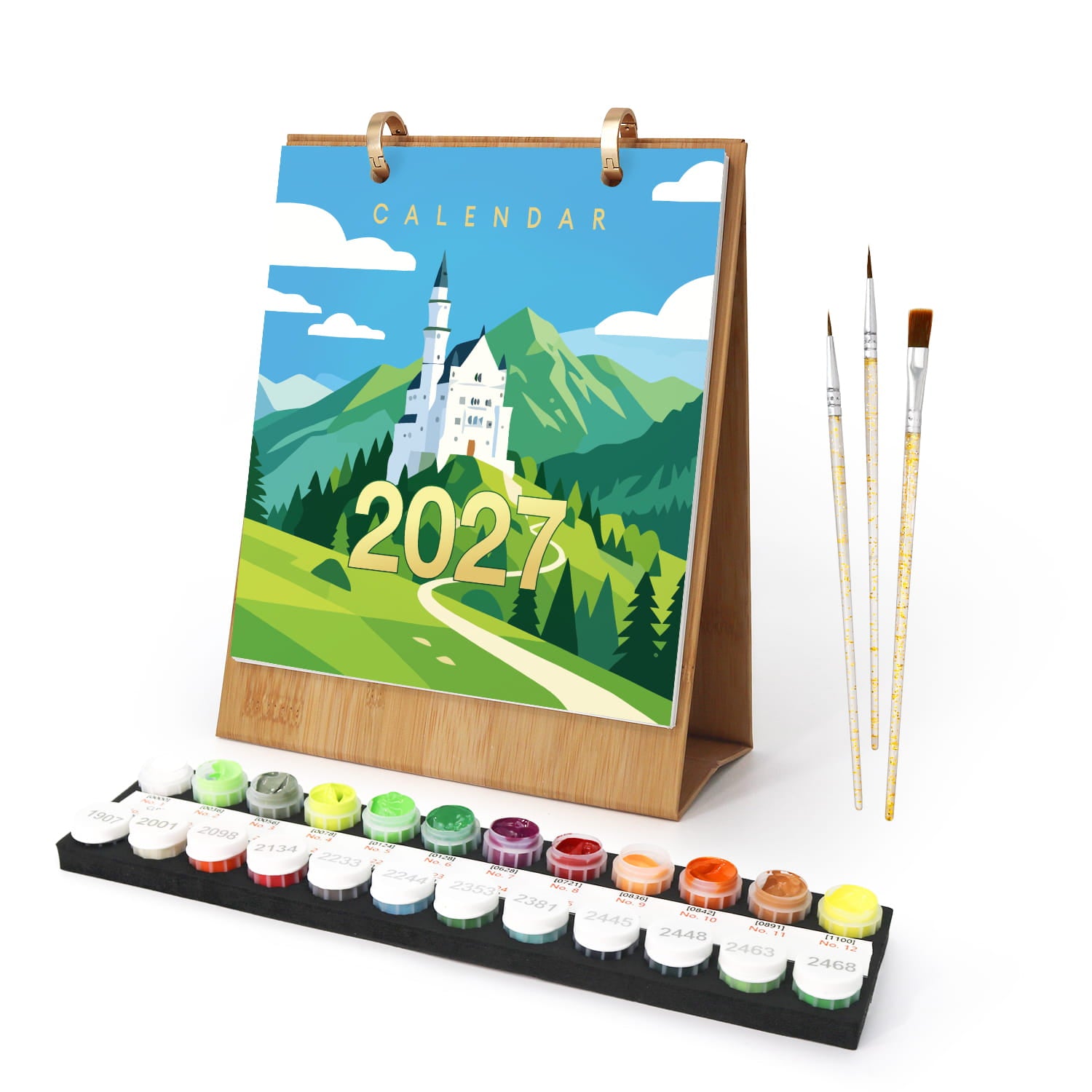 A 2027 wall calendar with a colorful landscape illustration of Neuschwanstein Castle, shown standing on a wooden base next to a set of paint pots and three paintbrushes on a white background.