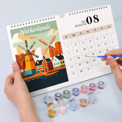 A spiral-bound Netherlands desk calendar is held open by two hands on a light gray surface. The left page shows a colorful illustration of Dutch windmills and houses with the word 'Netherlands' at the top.