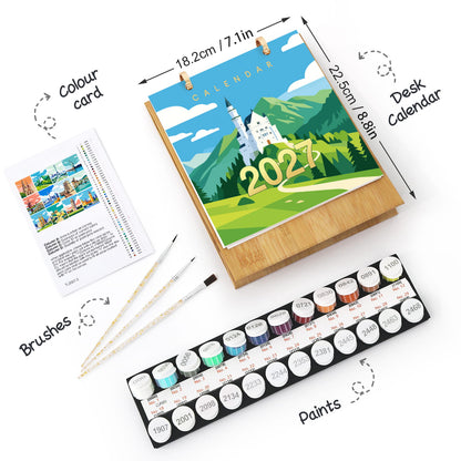 A desk calendar painting set shown on a white background with dimension labels and callout arrows. The set includes a wooden easel holding a colorful 2027 calendar, a colour card, two paintbrushes, and a tray of watercolor paints.