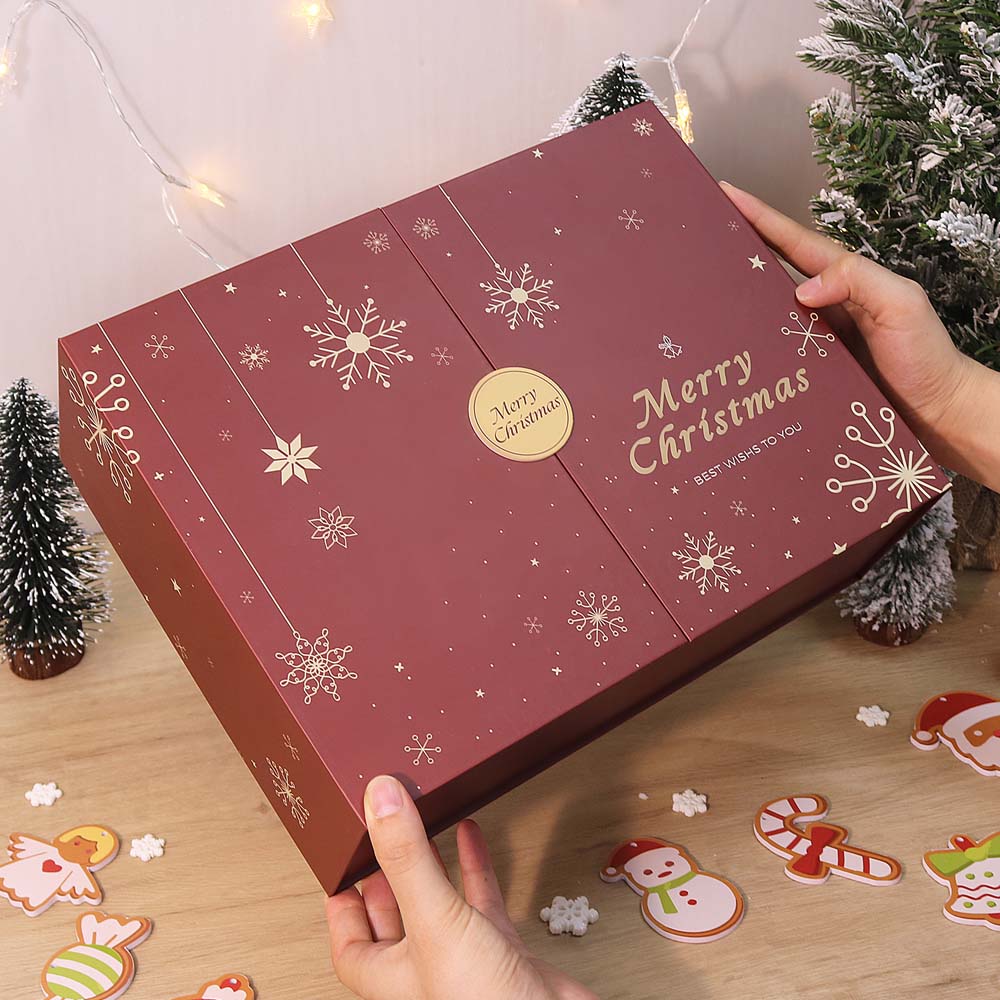 Red Christmas-themed box with snowflakes and 'Merry Christmas' text, held by a hand on a wooden surface with festive decorations.