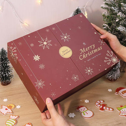 Red Christmas-themed box with snowflakes and 'Merry Christmas' text, held by a hand on a wooden surface with festive decorations.