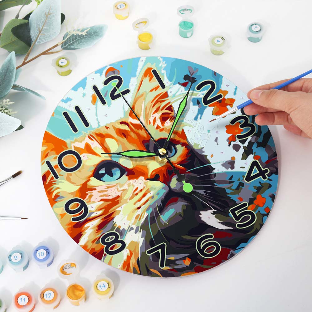 Colorful clock with a cat design being painted on a white surface with paint containers and brushes.